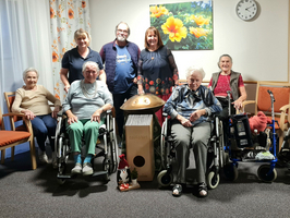 Eine Gruppe von sieben Personen, darunter Senioren, sitzt in einem Raum.