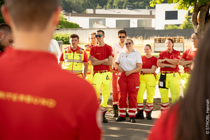 Gruppe von Rettungskräften in einheitlicher Kleidung, die einer Ansprache zuhört.