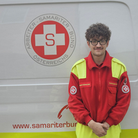 Ein Sanitäter in Uniform steht vor einem Rettungsauto des Samariterbundes.