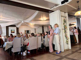 Frauen sitzen an Tischen in einem eleganten Restaurant, einige stehen in der Nähe.