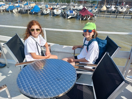 Zwei Mädchen mit Sonnenbrillen sitzen an einem Tisch auf einem Boot.