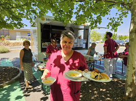 Eine Person in Rot serviert Essen vor einem Imbisswagen im Freien.
