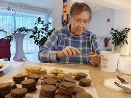 Eine ältere Person dekoriert Plätzchen auf einem Tisch voller frisch gebackener Kekse.