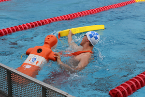Ein Schwimmer übt Rettungstechniken mit einer Übungspuppe im Wasser.