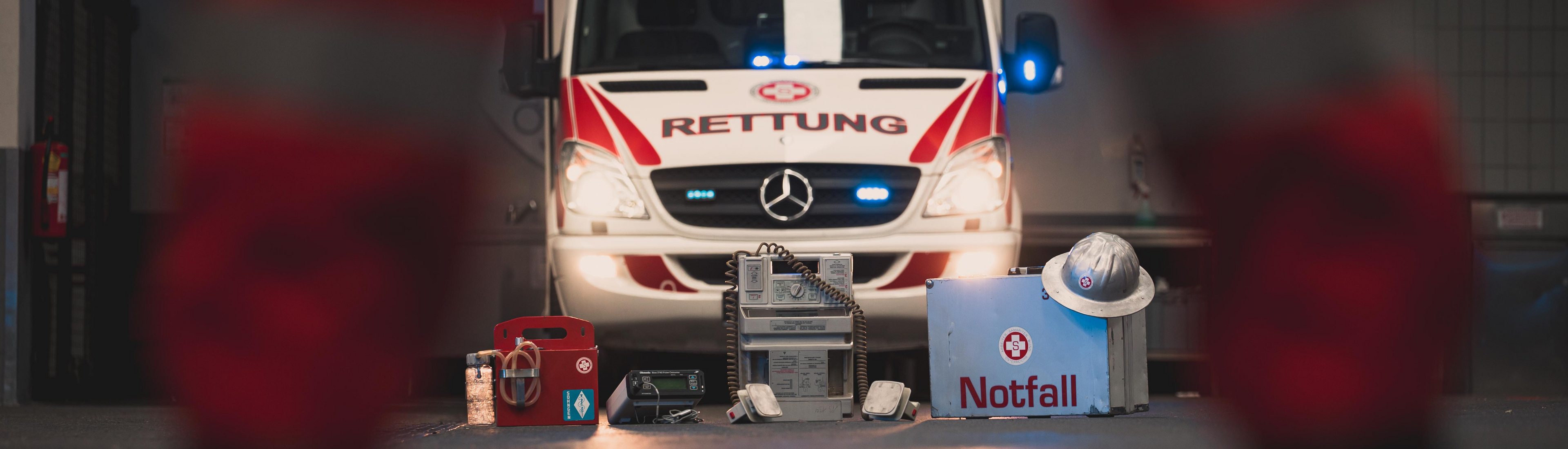 Notfallkoffer mit Helm, Defibrillator, dahinter KTW