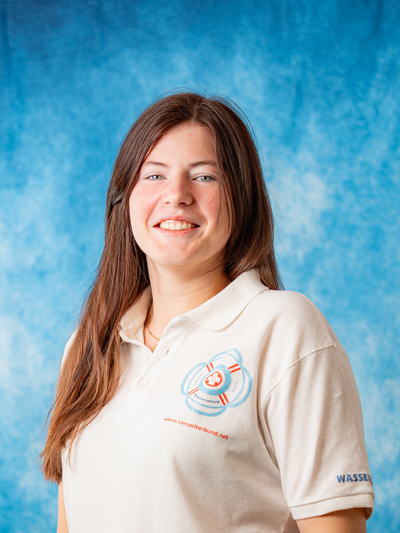 Junge Frau lächelt in einem hellen Poloshirt vor einem blauen Hintergrund.
