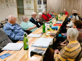 Ältere Menschen sitzen an einem Tisch und unterhalten sich bei einer Versammlung.