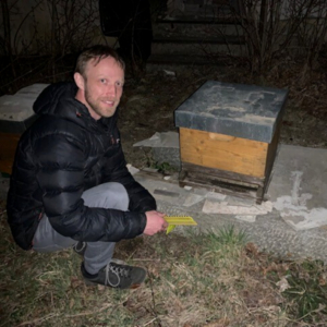 Nachtaufnahme Imker ohne Schutzausrüstung kniet vor Bienenstock, der auf erhöhter betonierter Plattform steht