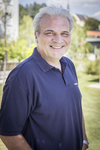 Ein lächelnder Mann in einem blauen Poloshirt steht im Freien.