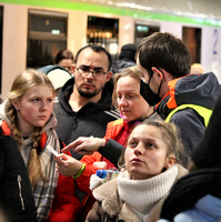 Menschen diskutieren an einer Bahnstation, während ein Mitarbeiter Anweisungen gibt.