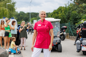 Eine lächelnde Frau in einem pinken Outfit steht auf der Straße.
