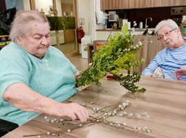Mehrere ältere Frauen in Rollstühlen halten Blumenarrangements und lächeln.