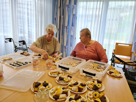 Zwei Frauen backen Gebäck an einem Tisch mit verschiedenen Plätzchen und Getränken.