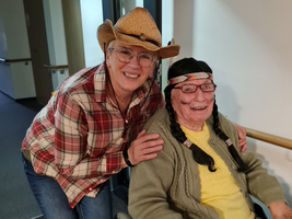 Eine Frau in Cowboy-Kluft lächelt neben einer älteren Frau im Rollstuhl.