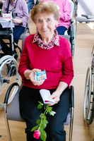 Ältere Frau sitzt mit einer Rose und einer Schokolade in der Hand.