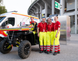 Rettungssanitäter:innen vor Stadion, eine Person sitzt auf Quad, dahinter Rettungsauto