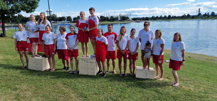 Gruppe von Sportlern auf dem Siegerpodest am Wasser.