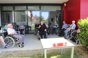 Gruppentreffen älterer Menschen im Freien, einige im Rollstuhl sitzend.