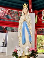 Statue einer betenden Maria mit Krone und Blumen um sie herum.