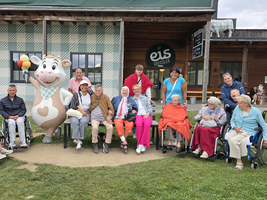 Gruppe von Senioren in Rollstühlen mit einem Maskottchen auf einer Wiese.