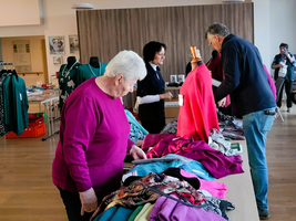 Menschen betrachten und sortieren Kleidung auf einem Tisch in einem Verkaufsraum.