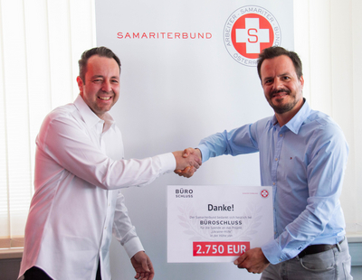 Zwei Männer schütteln sich die Hände und halten ein Dankesschild für eine Spende.
