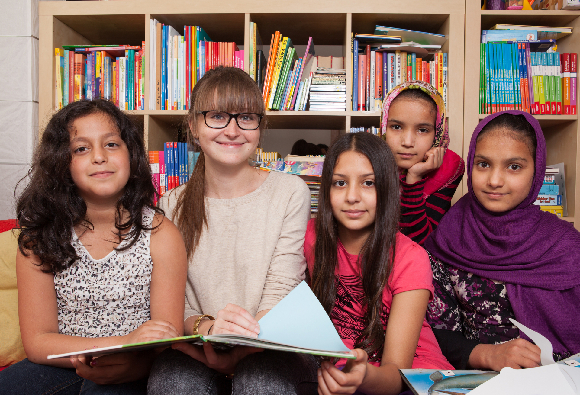 Fünf Mädchen sitzen zusammen und lesen Bücher in einer freundlichen Umgebung.