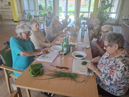 Ältere Frauen bereiten gemeinsam frische Lebensmittel an einem Tisch vor.