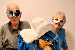 Zwei ältere Menschen mit Masken stehen neben einem kostümierten Dummy.