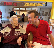 Junge hilft älterer Dame in einem Seniorenheim, freundliches Gespräch.
