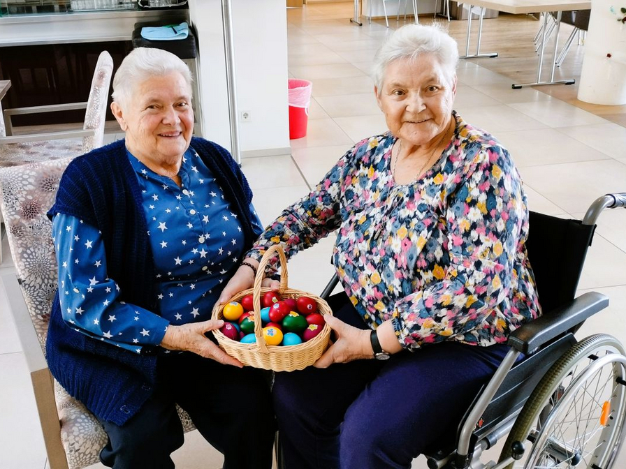 Zwei ältere Damen halten einen Korb mit bunten Eiern in der Hand.