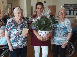 Drei Frauen stehen zusammen, eine hält einen Blumentopf, andere halten eine Karte.