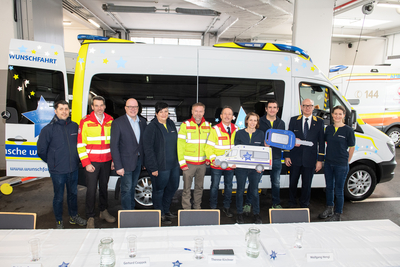 Eine Gruppe von Personen zeigt symbolisch einen Schlüssel zu einem Krankenwagen.