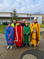 Fünf Personen in festlichen Kostümen stehen vor einem Gebäude.