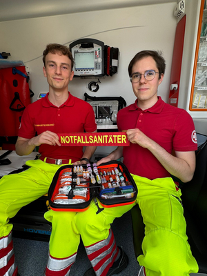 Zwei Notfallsanitäter zeigen eine Tasche mit medizinischem Zubehör.