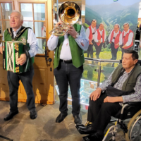 Drei Männer spielen traditionelle Musik, einer sitzt im Rollstuhl.