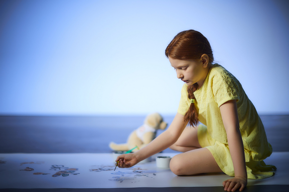 Mädchen sitzt am Boden und malt