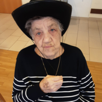 Eine ältere Frau mit einem schwarzen Hut und gestreiftem Pullover blickt ernst.