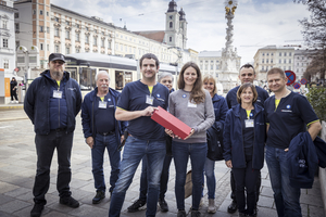 Eine Gruppe von Menschen steht lächelnd zusammen und hält eine rote Box.