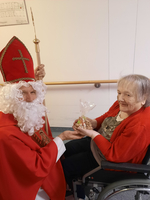 Der Nikolaus übergibt einer älteren Frau ein Geschenk in einer Einrichtung.