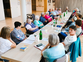 Eine Gruppe älterer Menschen sitzt an einem Tisch und führt ein Gespräch.