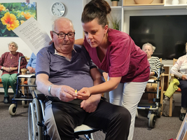 Eine Pflegekraft hilft einem Senior, eine Kerze anzuzünden.