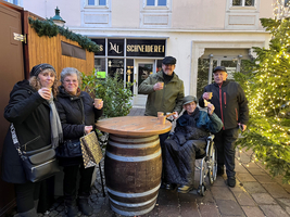 Sechs Personen stehen um ein Holzfass und stoßen mit Bechern an.