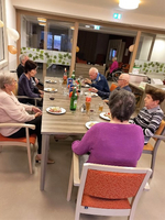 Eine Gruppe älterer Menschen sitzt um einen Tisch mit Essen und Getränken.