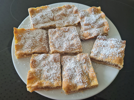 Ein Teller mit acht rechteckigen Kuchenstücken, bestreut mit Puderzucker.