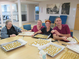 Menschen backen gemeinsam Plätzchen an einem Tisch in einer offenen Umgebung.