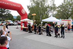 Rettungshunde und Beamte stehen vor einem Informationsstand bei einer Veranstaltung.