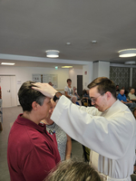 Ein Priester segnet eine Person durch Handauflegung in einem Raum.