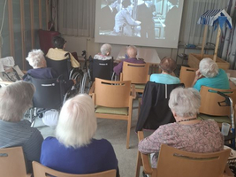Ältere Menschen schauen einen Film auf einer Leinwand in einem Gemeinschaftsraum.