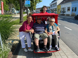 Vier Personen stehen und sitzen in einem Fahrzeug auf der Straße.